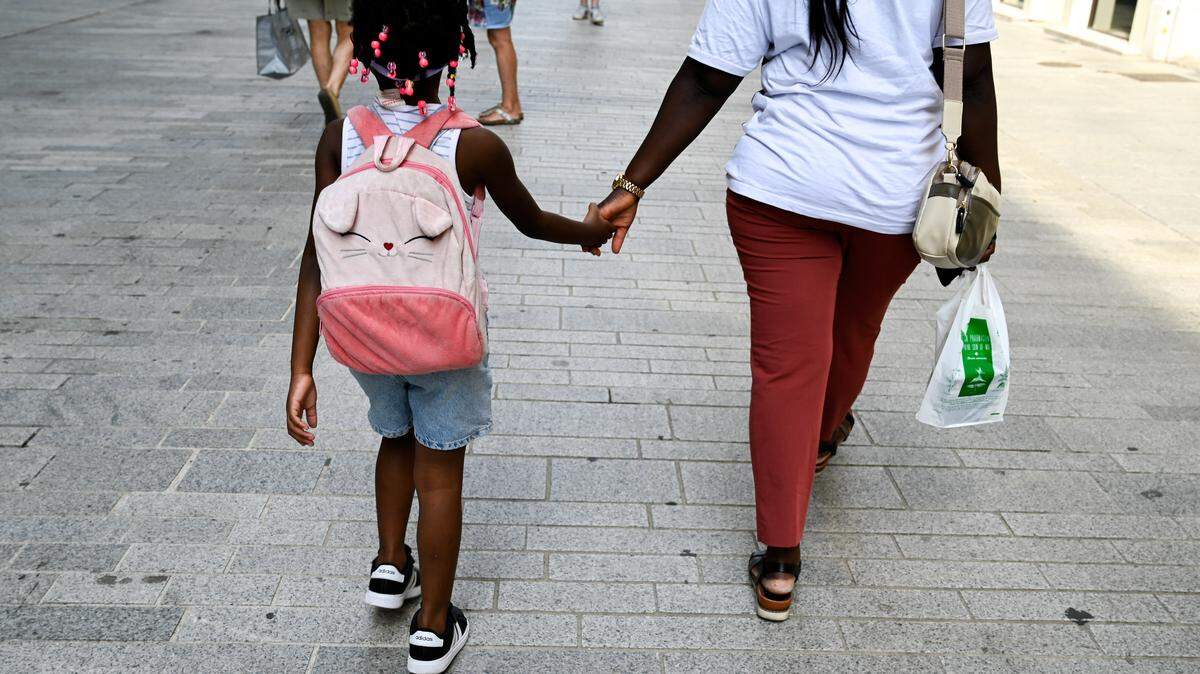 A mother holds the hand of her daughter carrying a backpack.