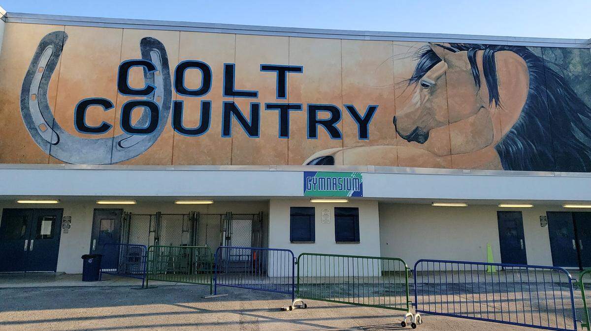An image of the Coral Springs High School Colts gymnasium exterior. It has a blue and orange mural that reads “Colts Country” with a horseshoe on the left and a horse on the right.