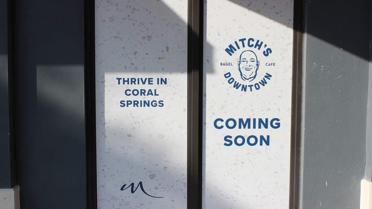 A sign on the future Mitch’s Downtown storefront includes the brand’s distinctive logo and Modera’s brand colors.