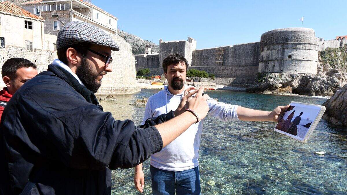 A guide hold up a picture of a “Game of Thrones” (GoT) scene in Dubrovnik while a tourist takes a photo of it.
