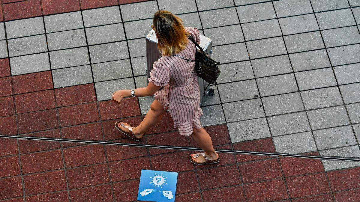A woman with a suitcase and purse walks past a floor sign, on the way to a coronavirus testing point, at Munich airport