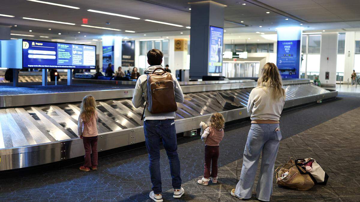 A mother, father, and two young daughters wait at baggage claim at an airport.