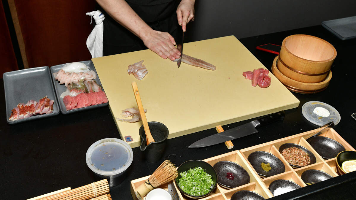 A chef slices fish at an omakase counter.