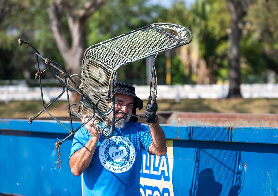 A volunteer at the 2025 waterway cleanup in Coral Springs lifts a rusted garden chair while smiling for a photo.
