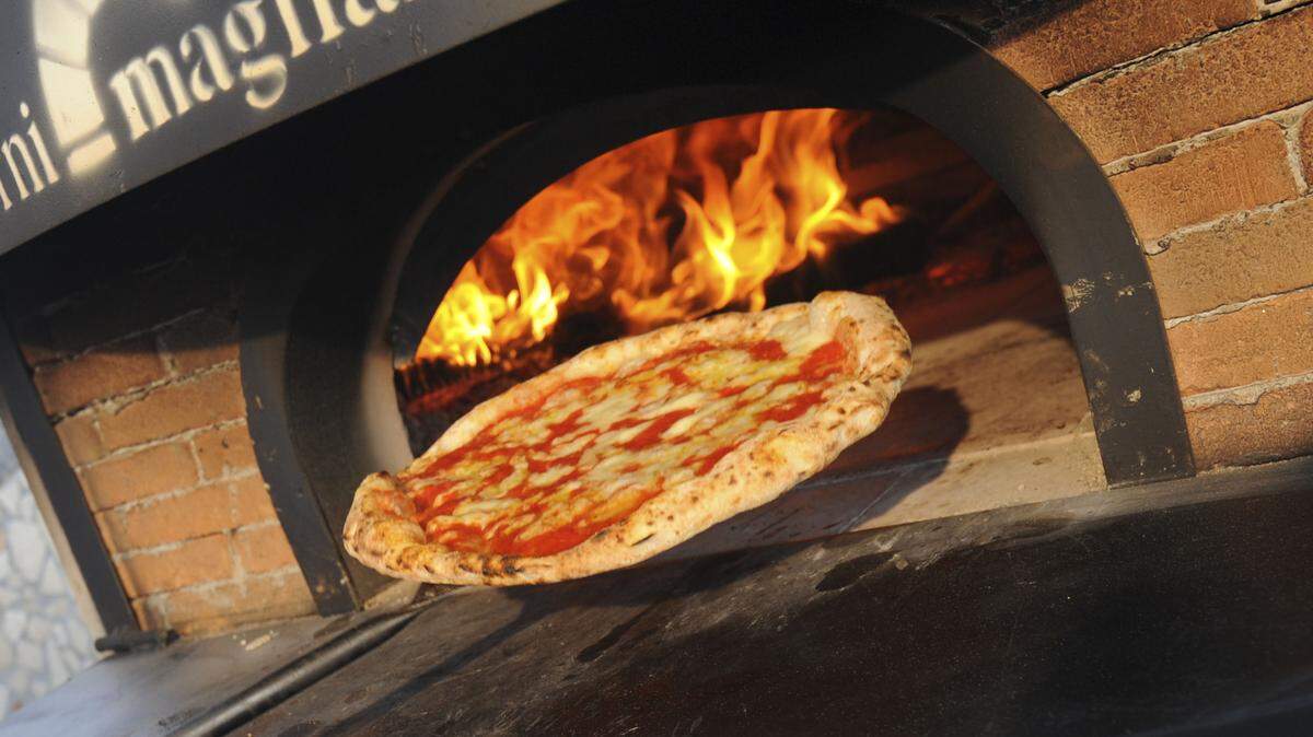 A pizza is removed from a wood-fired oven.