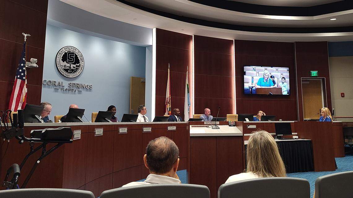 Coral Springs City Commission chambers with Commissioners, City Attorney, deputy City Clerk and deputy City Manager on dais while woman speaks at podium.