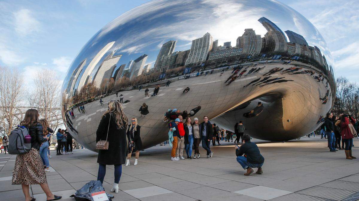 Groups of people standing together, taking pictures as they visit Cloud Gate statue, known as the “Bean”, in Millennium Park in Chicago, Illinois.