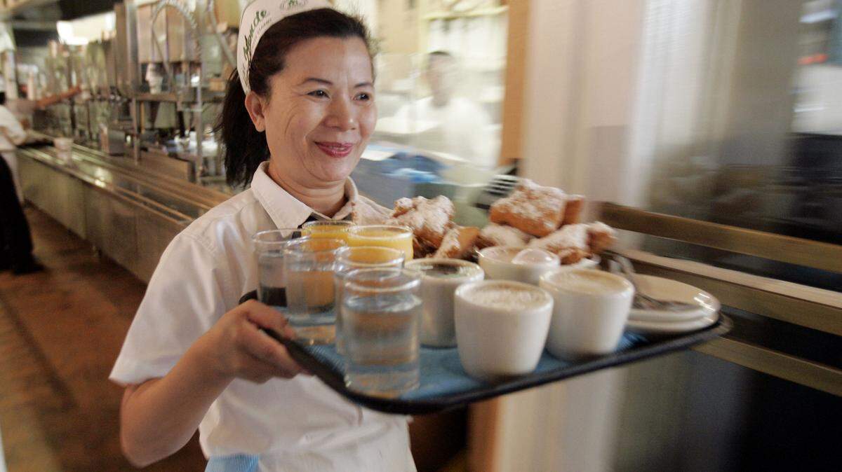 A waitress delivers an order of coffee and chicory and beignets at Cafe Du Monde in New Orleans, Louisiana.