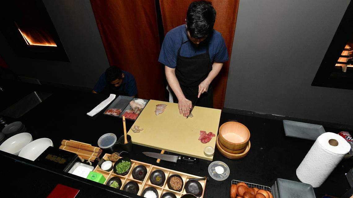A chef slices fish at an omakase counter.