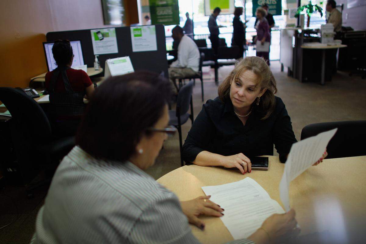 Two women sit across from each other at a table looking at paperwork together.