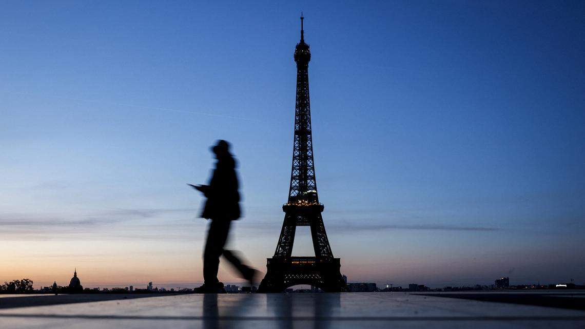 A pedestrian walks along the Esplanade du Trocadero with a view of the Eiffel Tower in the background at sunrise in Paris.