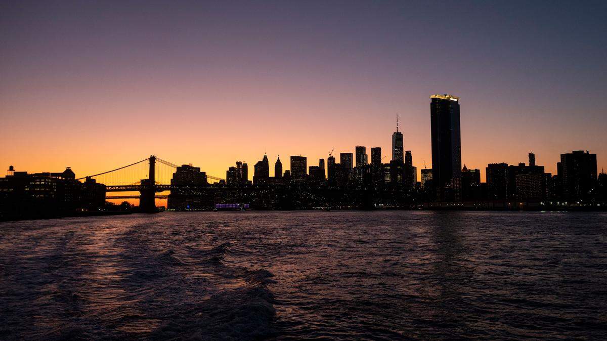 The sun sets behind the skyline of lower Manhattan in New York City.