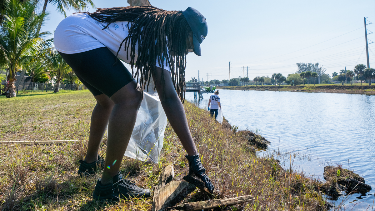 A volunteer gathers debris from a Broward canal embankment.
