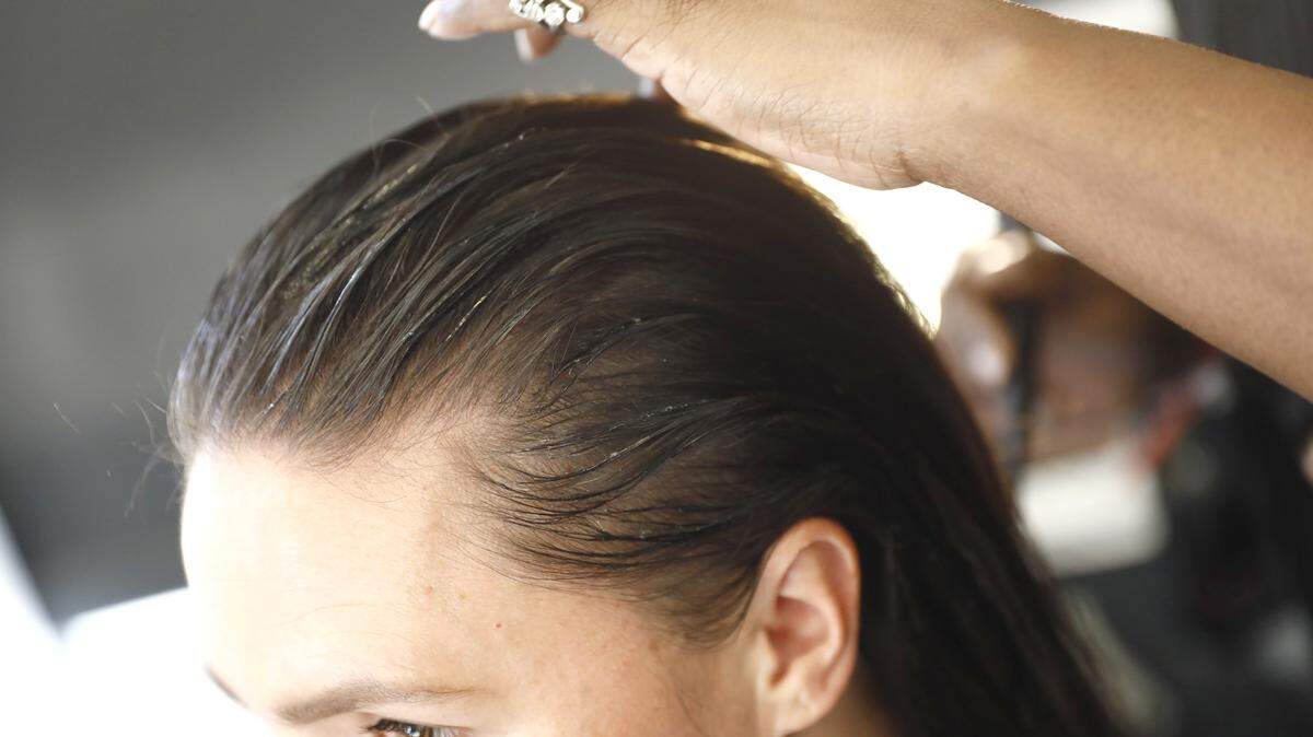 A stylist applies hair products to a woman.
