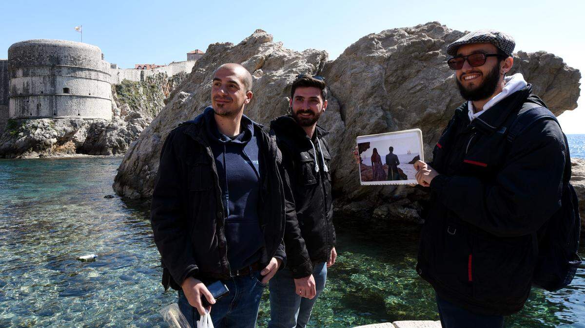 3 male tourists stand while one holds a picture of a “Game of Thrones” (GoT) scene during a guided visit to Dubrovnik.
