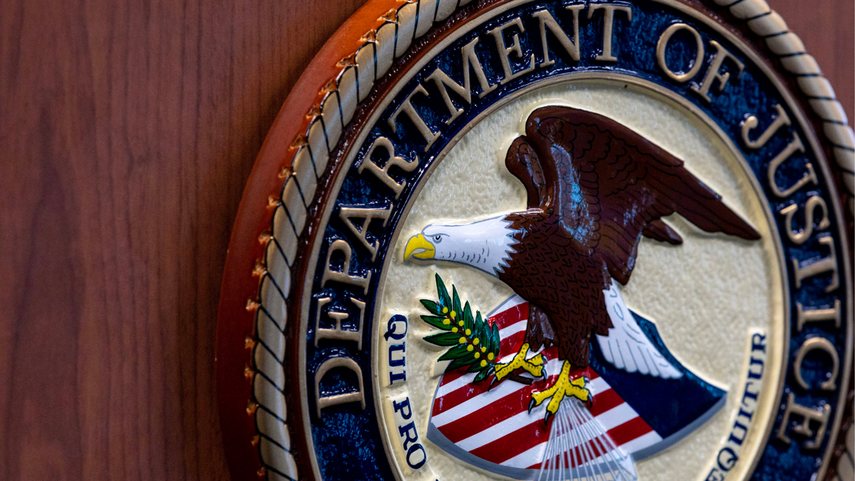 A close up of the Department of Justice insignia on a dark wood background. The image features a bald eagle.