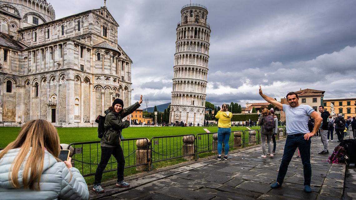 View of the Leaning Tower of Pisa with tourists taking photos of themselves pretending to support the tower in Pisa.