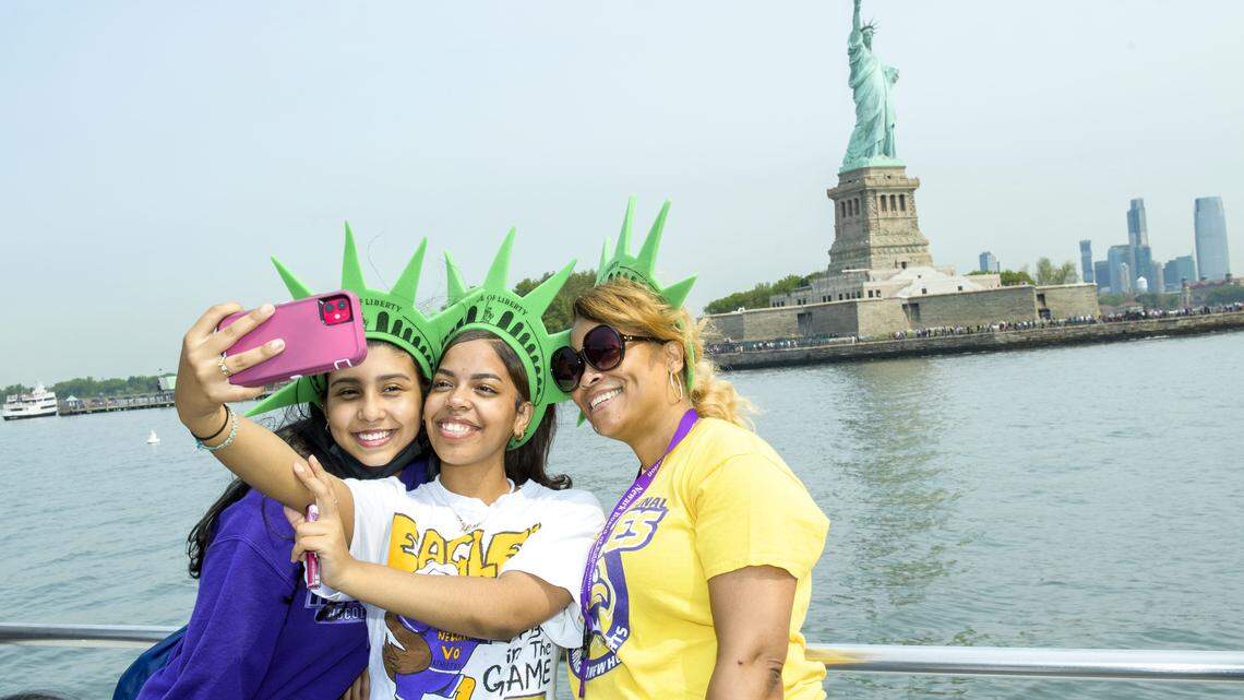 Tourists pose for photos on a boat passing the Statue of Liberty in NYC