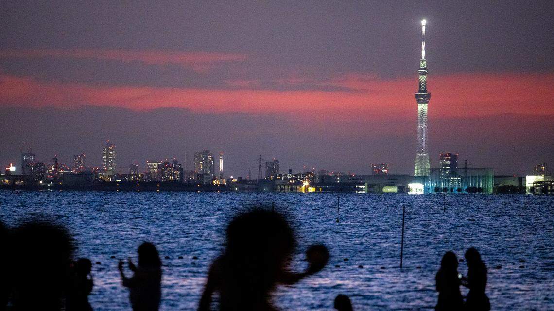 People gather on the beach as the Tokyo Skytree is seen in the background .