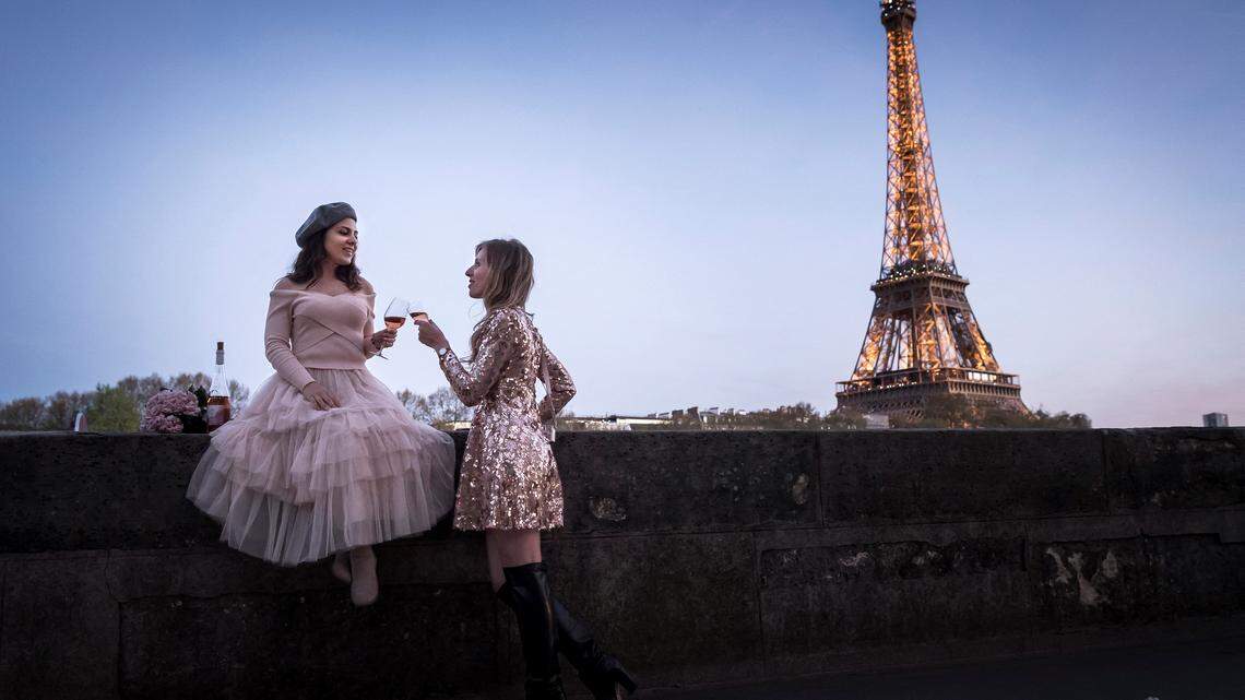 Two female tourists drink glasses of wine together near the Eiffel tower on April 17, 2018, in Paris.