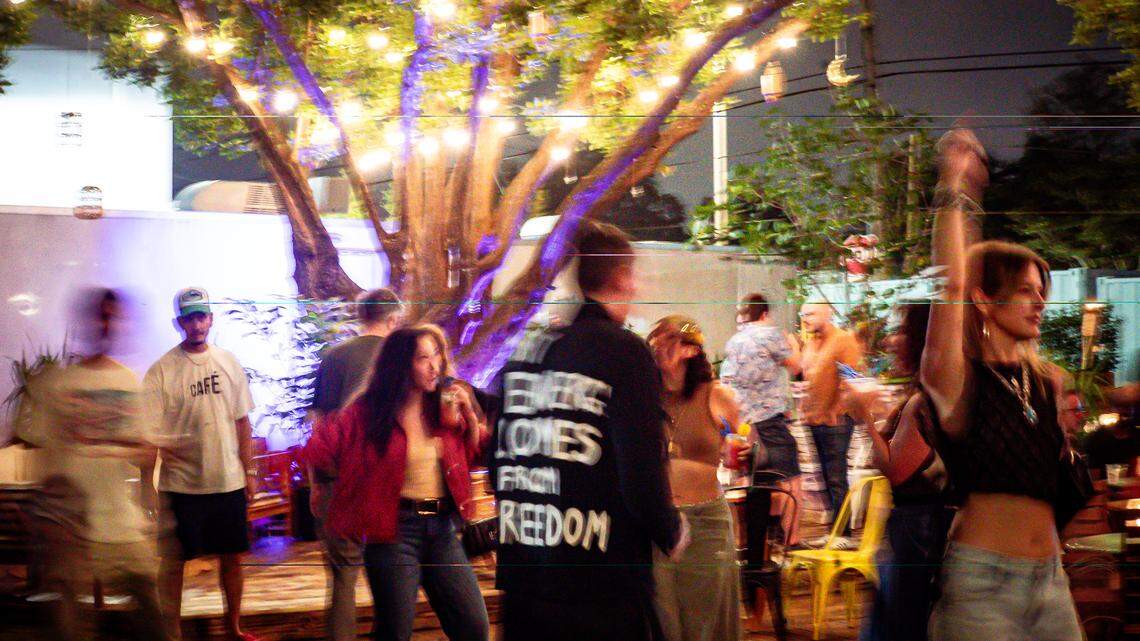 A crowd of people dancing under trees lit up with string lights at The Triangle Little River in Miami.