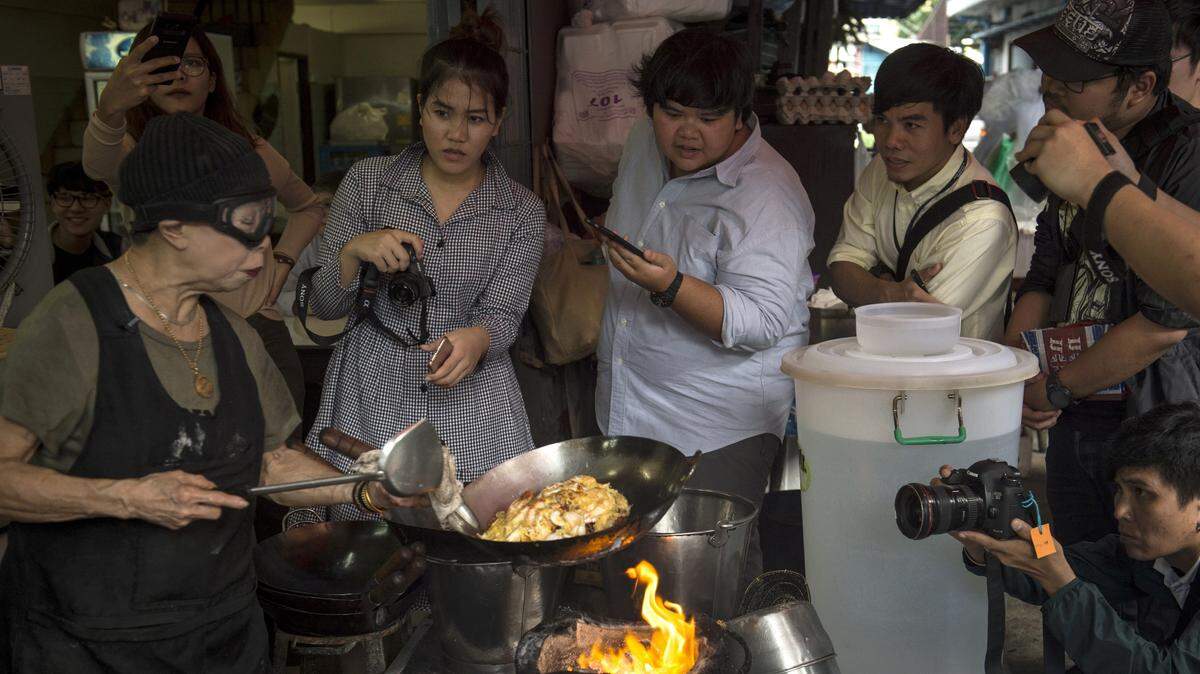 Members of the media watch as Chef Jay Fai cooks in her kitchen wearing her trademark goggles.