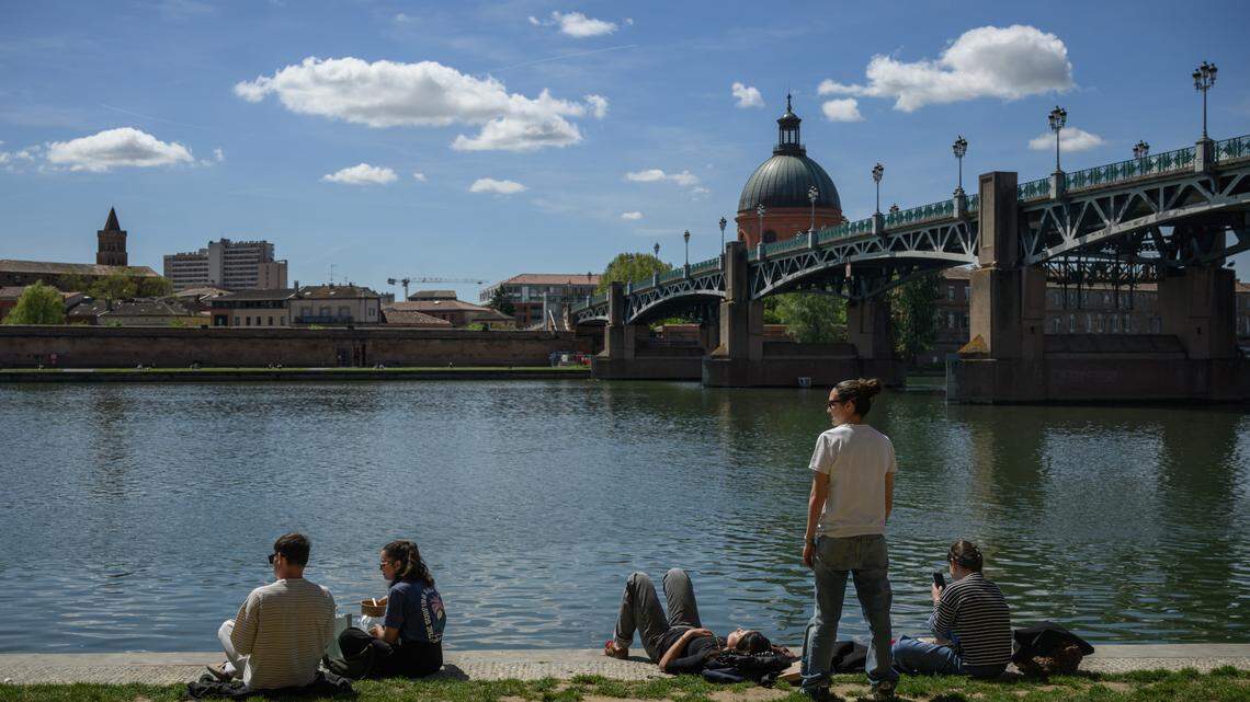 People sit on the banks of the Garonne river with a view of the Chapelle Saint-Joseph de la Grave in Toulouse.