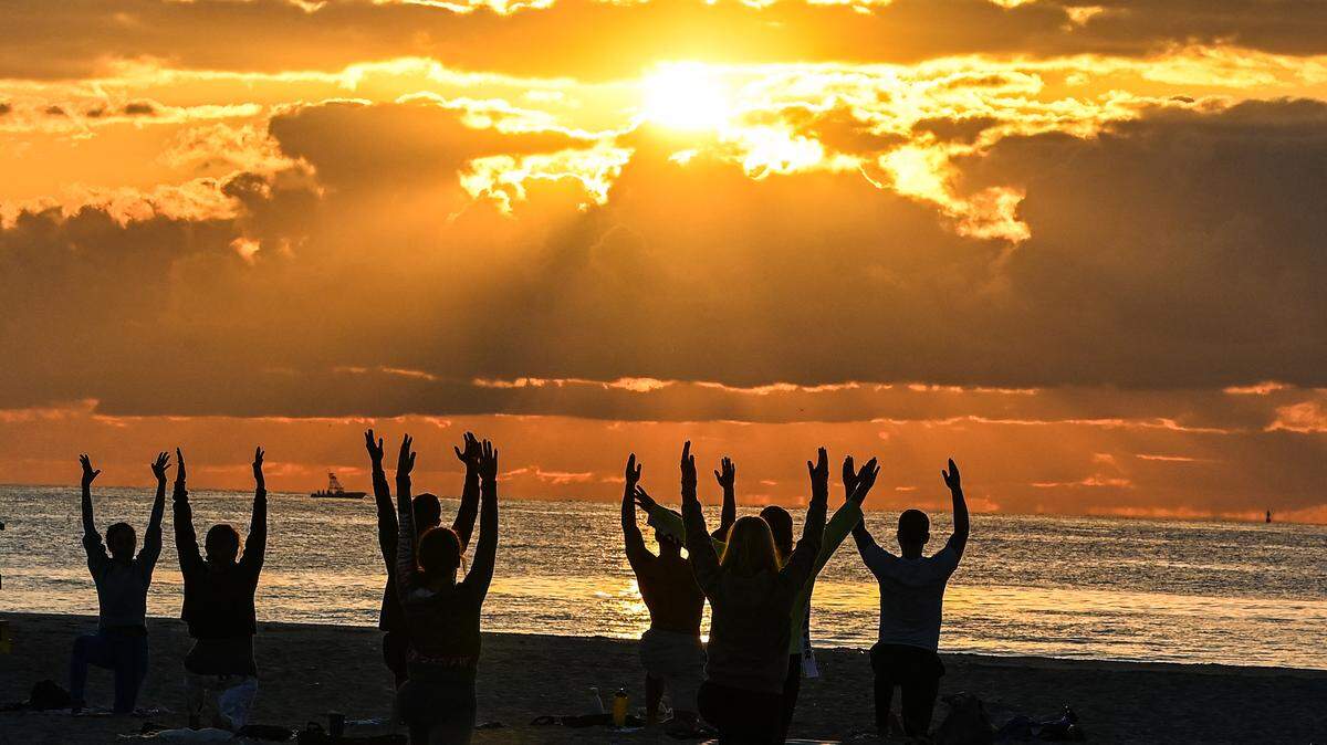 A group of people participate in a yoga session on the beach.