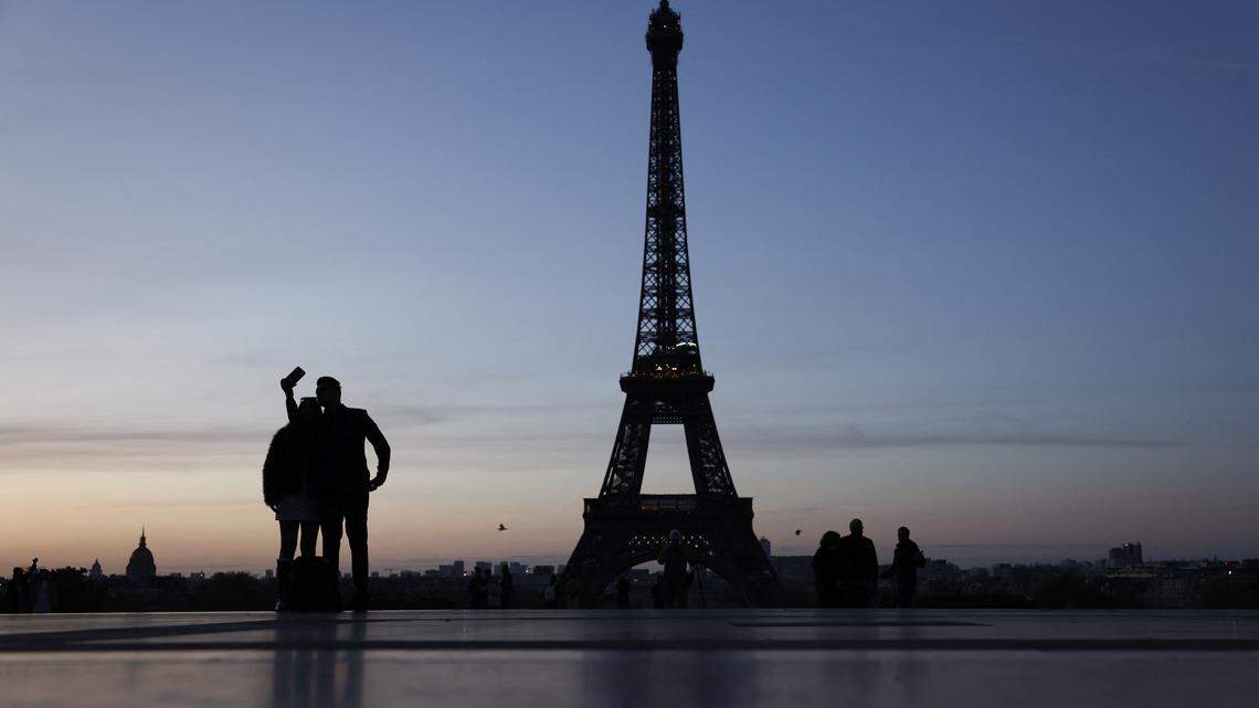 Two people take a selfie at the Trocadero in front of the Eiffel Tower at sunrise in Paris.
