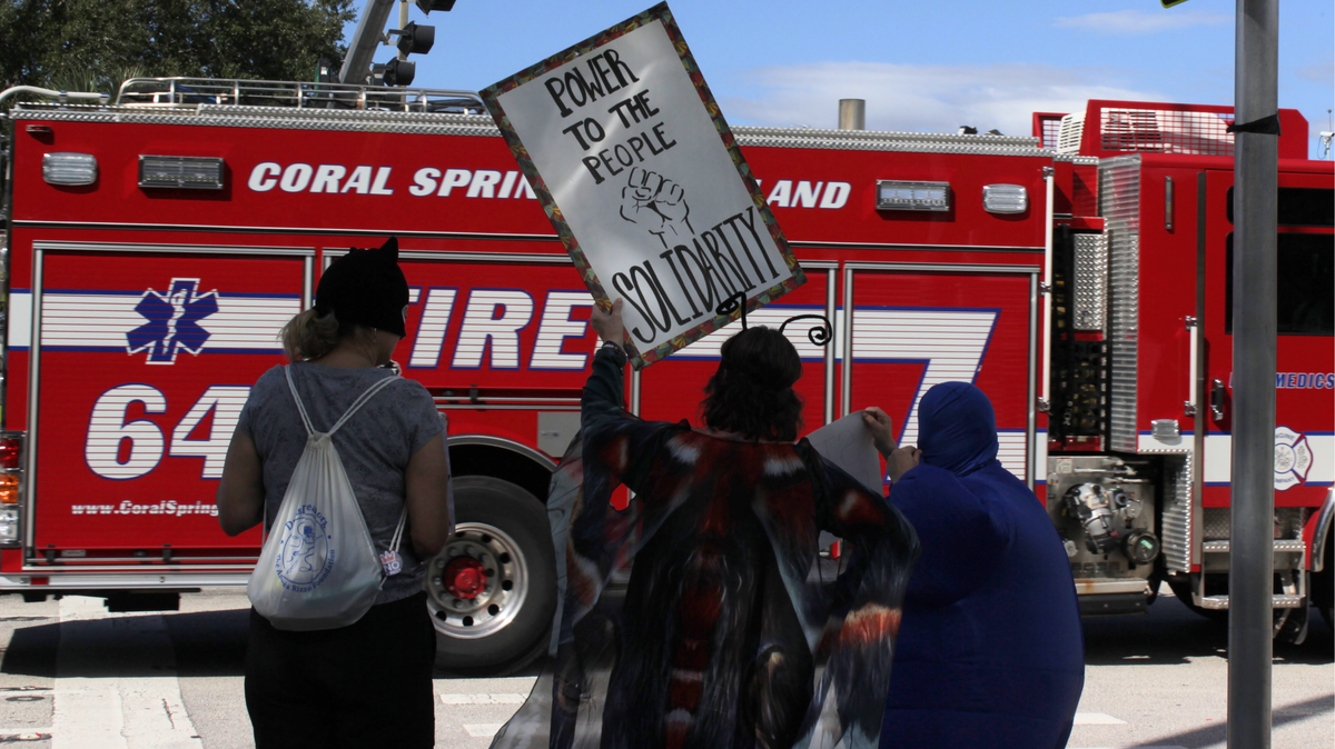 A handful of residents from the Coral Springs area gathered to protest what they saw as an illegal threat of arrest by a Coral Springs police officer, as well as actions by President Donald Trump’s administration.