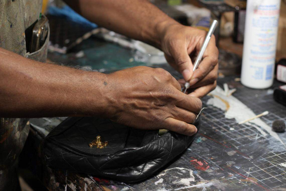 Hands, holding a silver craft knife, cut into a small black designer purse.