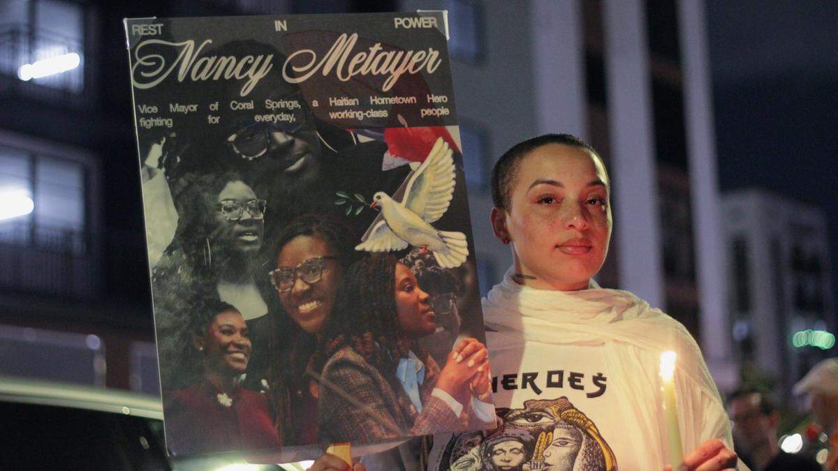Athena Guice, 30, stands for a photo with her sign and lit candle after the April 3, 2026 vigil for Coral Springs Vice Mayor Nancy Metayer.