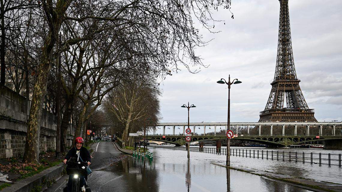 A cyclist rides near the banks of the Seine river with the Eiffel Tower in the background