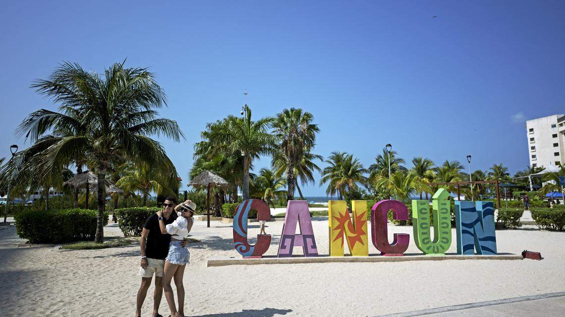 A couple takes a selfie in front of a large sign reading “CANCUN” at a beach in Cancun, Mexico.