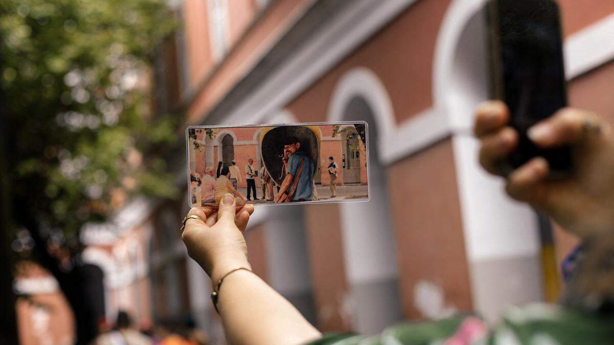 A tourist holds a photo showing a scene from a film against the backdrop of where it was filmed during a guided tour.