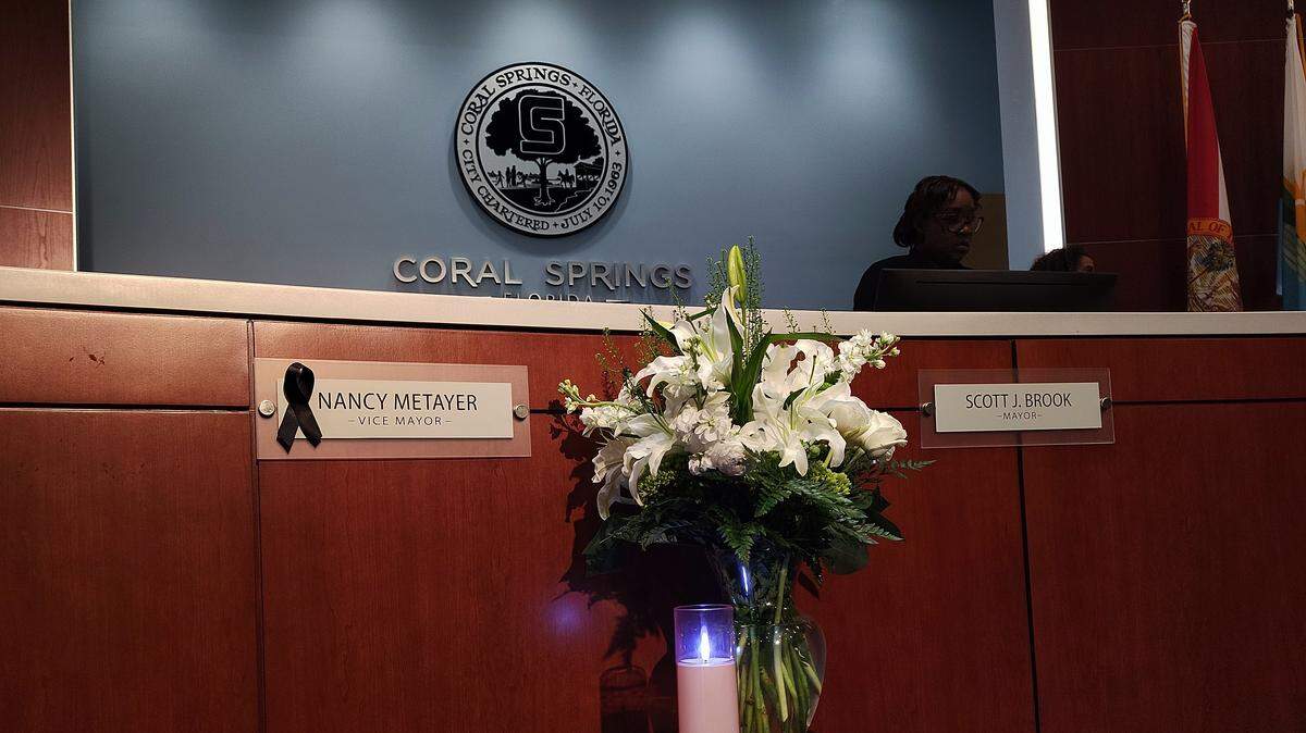 Coral Springs Vice Mayor Nancy Metayer Bowen’s seat sat empty at the first City Commission meeting since she was found dead in her home, allegedly murdered by her husband. As of April 14. her nameplate has been updated to reflect her maiden name, and an electric candle and bouquet of flowers sit in front of her place on the dais.
