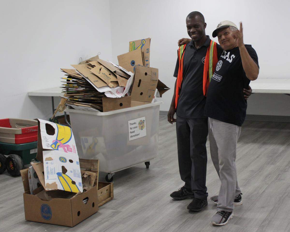 Volunteers Robenson Altidor and Manuel Rivera pose for a photo in front of broken-down cardboard boxes after the Royal Palm food pantry closed its doors for the night.