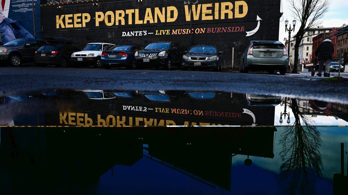A Keep Portland Weird mural on Dante’s is reflected in a puddle of water near Burnside Street in Portland, Oregon.