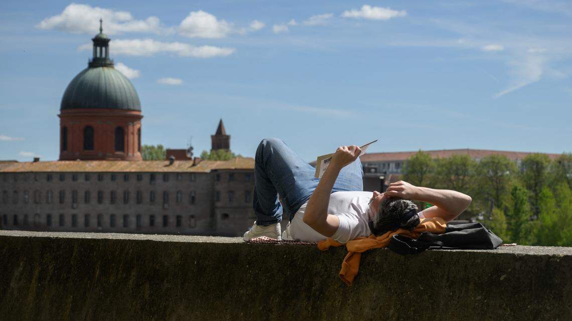 A man reads a book on a wall beside the Garonne river with a view of the Chapelle Saint-Joseph de la Grave in Toulouse.