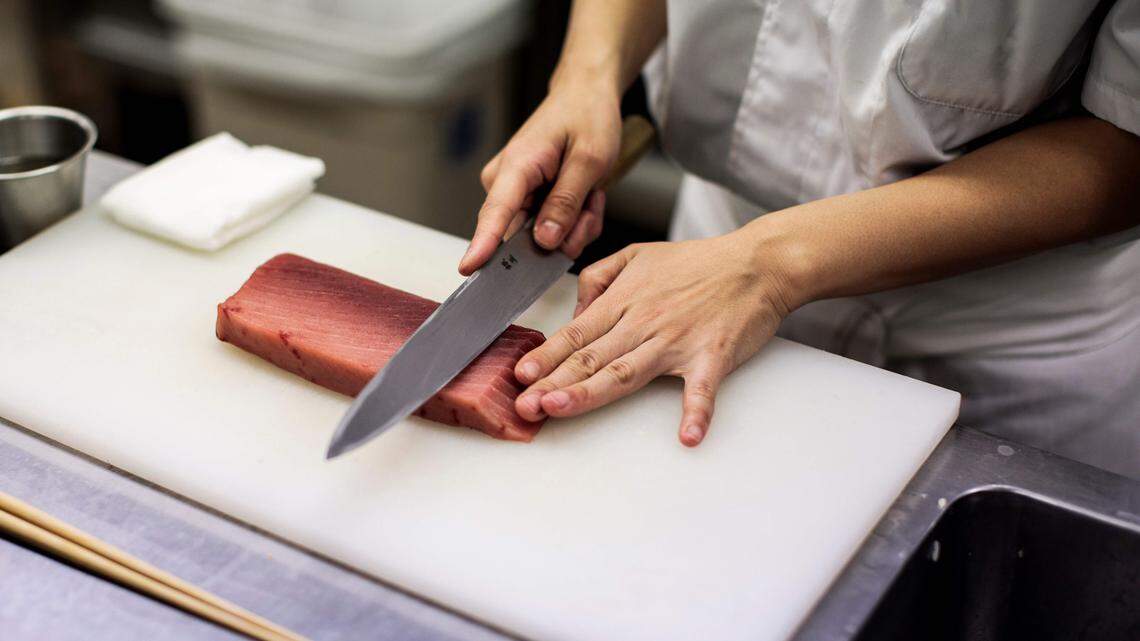 A sushi chef cuts a fish fillet to make sushi.