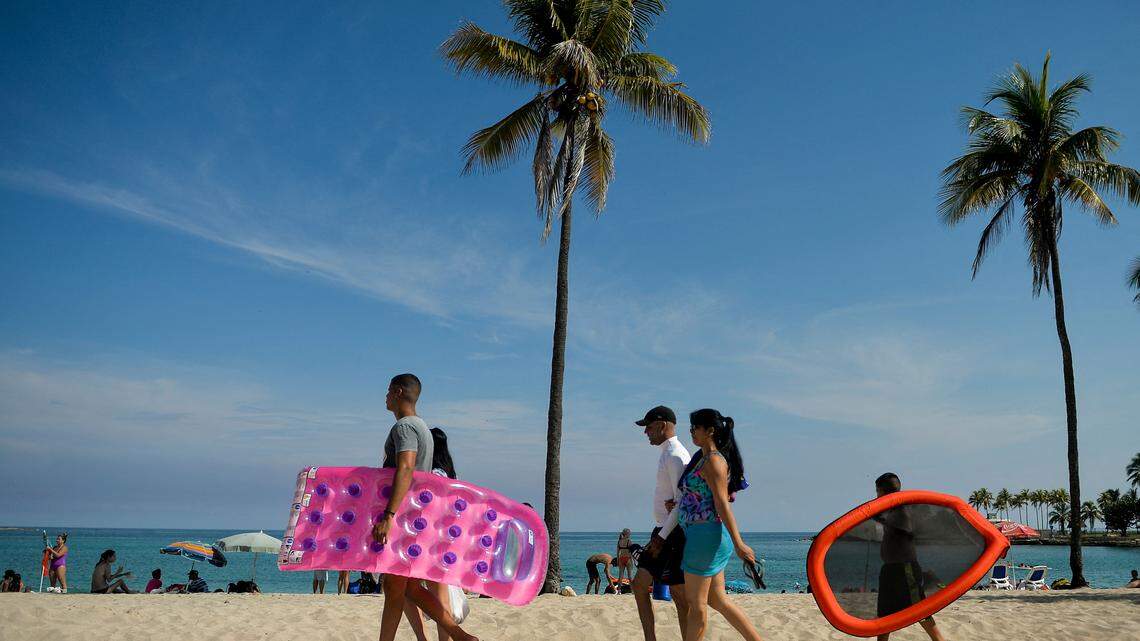 A Cuban family arrives at Bacuranao beach in Havana carrying floaties with palm trees in the background.