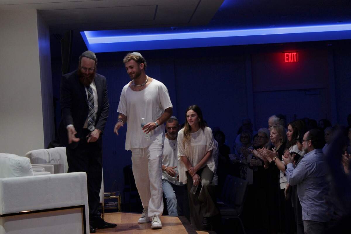 Rabbi Yankie Denburg, left, guides Itay Regev, center, and Maya and Ilan Regev, right, onto the stage at Chabad of Southwest Coral Springs as the audience applauds.