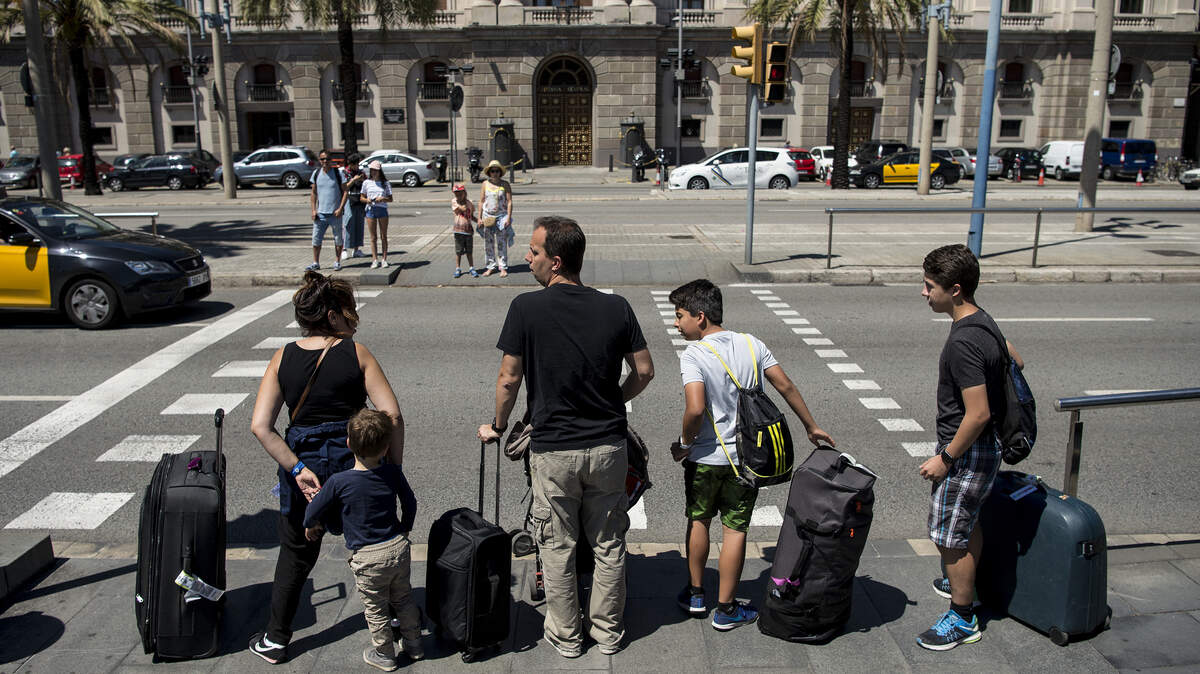 A family of tourists stand at a crosswalk with their bags.