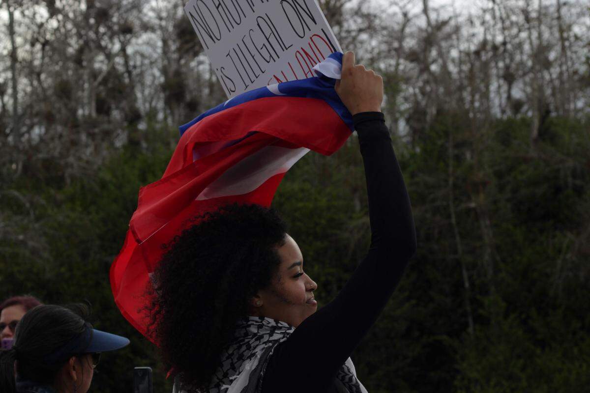 Deemaris Young stands with a sign reading “No human is illegal on stolen land” during a protest and vigil for the detainees at Alligator Alcatraz on March 1.