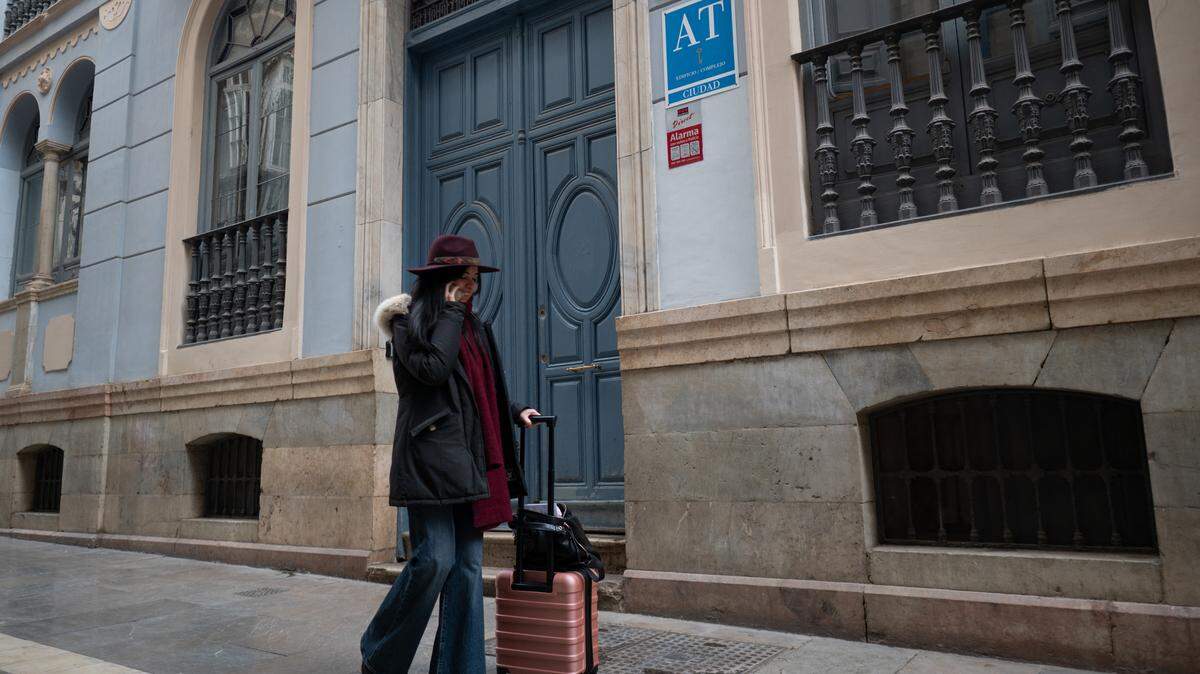 A woman pulls her luggage on the sidewalk.
